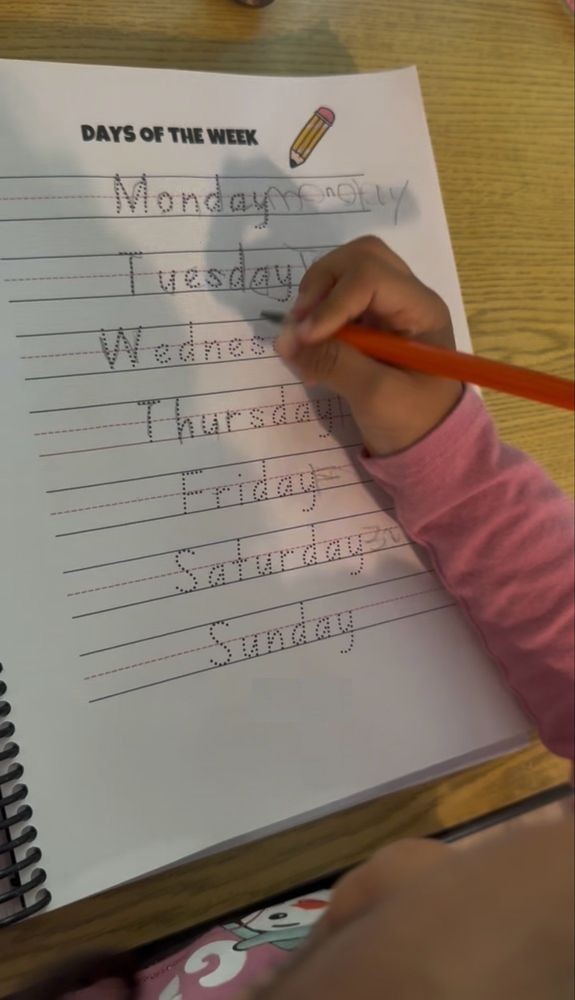 A child tracing the days of the week in a handwriting workbook