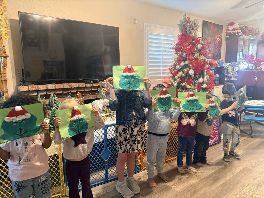 Seven children standing in a row holding up handmade Grinch crafts they painted, in a living room decorated for the holidays